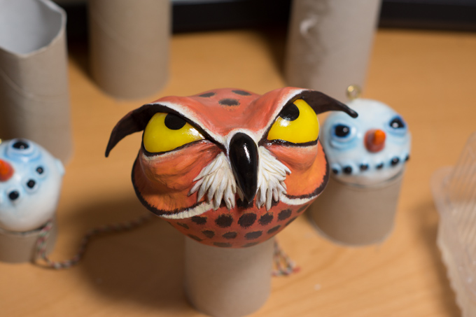 the owl ornament painted. It is looking upward in an annoyed kind of way. Two ornaments of snowmen in the background
